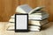 Portable e-book reader and open hardcover books on wooden table