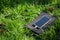 Portable solar battery and mobile phone on green grass. Charging electronic gadgets on a hike, during outdoor recreation.