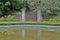 A portal with two columns in the middle of the bushes. Opposite gardens and a small pond. Sao Paulo Botanical Garden