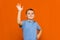 Portarait of caucasian happy smiling little boy with raised hand on orange wall