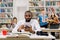 Portarit of young concentrated young african male bearded student in white shirt, studying in library with his friends