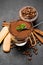 Portion of Classic tiramisu dessert in a glass cup, scoop full of coffee and cinnamon sticks on dark concrete background