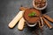 Portion of Classic tiramisu dessert in a glass cup, scoop full of coffee and cinnamon sticks on dark concrete background