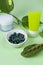 Portion green capsules for skin health, two face cream tube near plant leaf on green background. Woman's care, detox