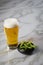 Portion Japanese Edamame soy beans in porcelain bowl with beer glass on marble background