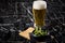 Portion Japanese Edamame soy beans in porcelain bowl on wooden board with beer glass on napkin and black marble background