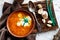 A portion of red borscht in a brown plate, next to an old wooden Board garlic and quail egg, green leeks and driftwood. White sour