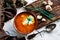 A portion of red borscht in a brown plate, next to an old wooden Board garlic and quail egg, green leeks and driftwood. White sour