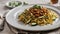 portion of tagliatelle rye and courgette with meat sauce in a white plate on wooden table