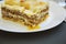 Portion of traditional lasagne served on a white round plate, dark background. Side view.