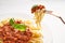 Portion Traditional pasta bolognese on a fork, served on a white plate and garnished with basil