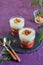 Portioned dessert in a glass with rhubarb jam, shortbread crumble and custard on a purple concrete background. Rhubarb recipes.