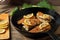 Portioned pieces of fried fish in a black cast-iron pan with fresh cucumbers and herbs. Traditional dinner of a village