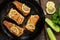 Portioned pieces of fried fish in a black cast-iron pan with fresh cucumbers and herbs. Traditional dinner of a village