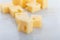 Portions cubes, dice of Emmental Swiss cheese with scratcher. Texture of holes and alveoli. On white marble background