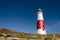 Portland Bill lighthouse at the top of the cliffs against a clear blue sky, Portland, Dorset, UK