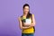 Portraif of asian student girl with backpack and workbooks over purple background