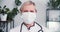 Portraif of happy senior Caucasian female doctor posing at office in protective face mask, white coat and stethoscope.