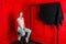 Portraint of woman sits on a chair with red background, looks into a camera
