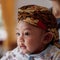 A portrait of a 3-month-old baby showing a smile and wearing Blangkon. Blangkon is a typical head covering of Java island made of