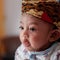 A portrait of a 3-month-old baby showing a smile and wearing Blangkon. Blangkon is a typical head covering of Java island made of