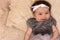 Portrait of a 4 month cute baby girl, wearing white headband and grey dress, lying down on a bed pillows