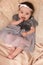 Portrait of a 4 month cute baby girl, wearing white headband and grey dress, lying down on a bed pillows