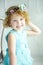 Portrait of 5 years old curly blonde smiling girl in blue dress and wreath. Spring coming little girl portrait in studio. Waiting