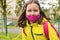 Portrait of a 9-year-old girl in a yellow jacket and pink mask with a pink briefcase. Children go to school in September