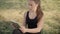 Portrait of absorbed young woman sitting on sunny meadow and surfing Internet on tablet. Beautiful Caucasian lady using