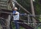 Portrait active kid climbing on rope frame at treehouse.Young boy standing alone and looking up at high forest tree near the park