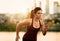 Portrait of active millenial woman jogging at dusk with an urban cityscape and sunset in the background