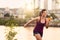 Portrait of active millenial woman jogging at dusk with an urban cityscape and sunset in the background