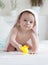 Portrait of adorable 9 months old baby boy covered in towel holding yellow rubber toy after washing in bath