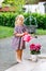 Portrait of adorable, charming toddler watering flowers with water can. Smiling happy child on summer day with colorful