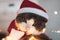 Portrait of adorable grey and white cat in red santa hat with cristmas lights