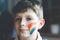 Portrait of adorable school kid boy with painted rainbow with colorful colors on face. Lonely child during pandemic