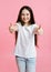 Portrait of adorable smiling little girl child in the white t-shirt with two fingers up isolated on a pink