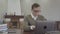 Portrait adorable young man in glasses sitting at the wooden table in the office, many books are on the table. Cute nerd