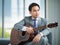 Portrait adult asian businessman very handsome and smart wearing suit relaxing by playing guitar feel casual and relaxation in