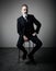 Portrait of adult businessman wearing trendy suit and sitting studio on chair against the empty wall. Vertical