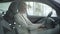 Portrait of adult Caucasian businesswoman in elegant white suit sitting on driver`s seat in car dealership. Happy