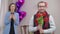 Portrait of adult Caucasian stylish man in eyeglasses posing with bouquet of flowers indoors with blurred excited woman