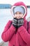 Portrait of an adult Caucasian woman dressed warm red jacket with hood on her head and knit mittens standing on quay of frozen