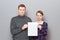 Portrait of adult couple holding together white blank paper sheet