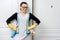 Portrait of adult positive smiling woman in glasses and apron for cleaning rubber gloves with detergents, white door background,