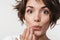 Portrait of affable woman with short brown hair in basic t-shirt covering her mouth with hand