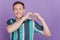 Portrait of affectionate guy fingers demonstrate heart symbol on purple background