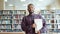 Portrait of African American student walking in university library with books