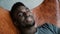 Portrait of African man sitting in chair, smiling and looking straight at camera. Male looks dreamy, thoughtful and calm